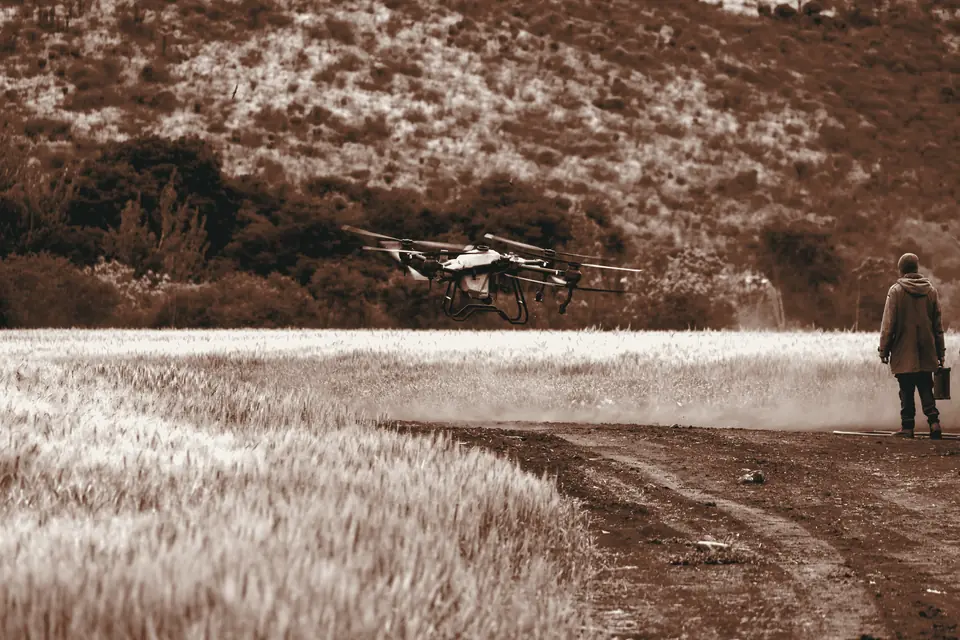 Drone agrícola sobrevoa uma plantação enquanto um agricultor acompanha o voo